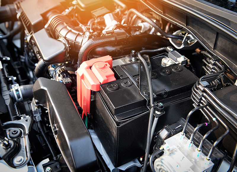 Close-up of a vehicle battery installed in the engine compartment, highlighting key engine components under the hood.